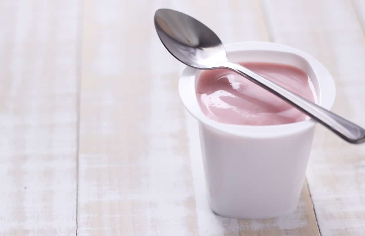 Plant-based-yogurt strawberry yogurt in white plastic cup with spoon on wooden white background.