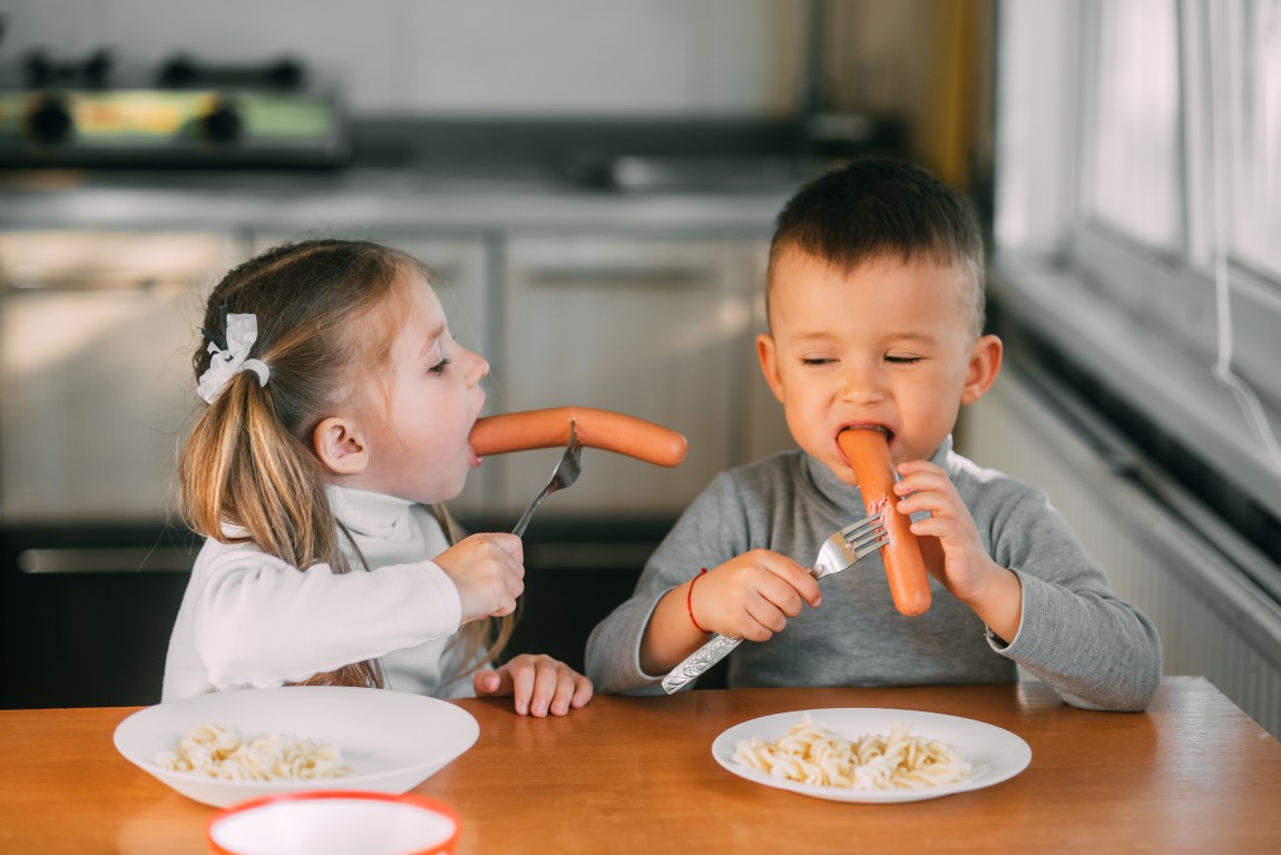 Les marchés rééquilibrent le profil nutritionnel Garçons et filles dans la cuisine mangeant des saucisses