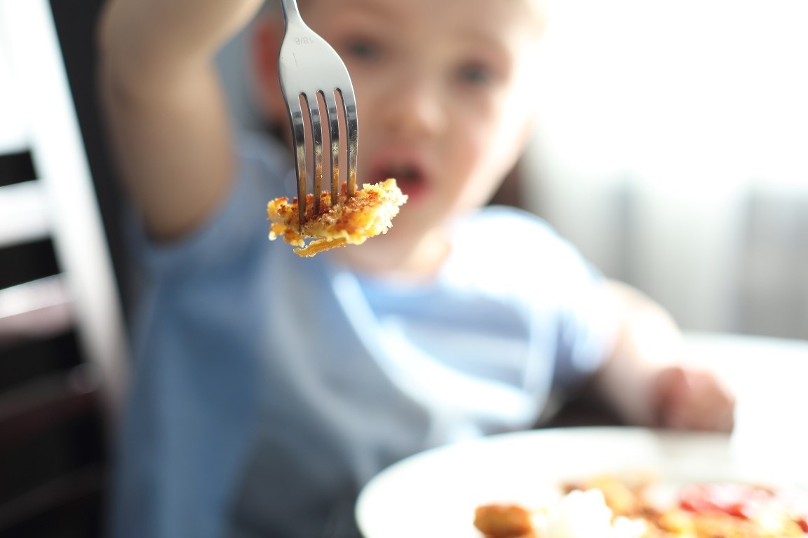 Enfant en mangeant. Le petit garçon lors d'un repas montre une côtelette estampée sur une fourchette.